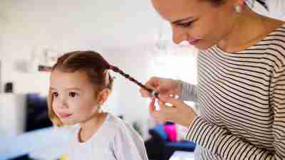 A mom braids her daughter's hair as part of their morning routine