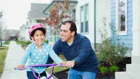 Father using positive parenting techniques to help his daughter learn how to ride a bicycle