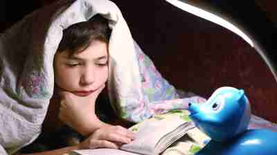 ADHD teen boy engaged in intriguing reading book under the blanket in night hour